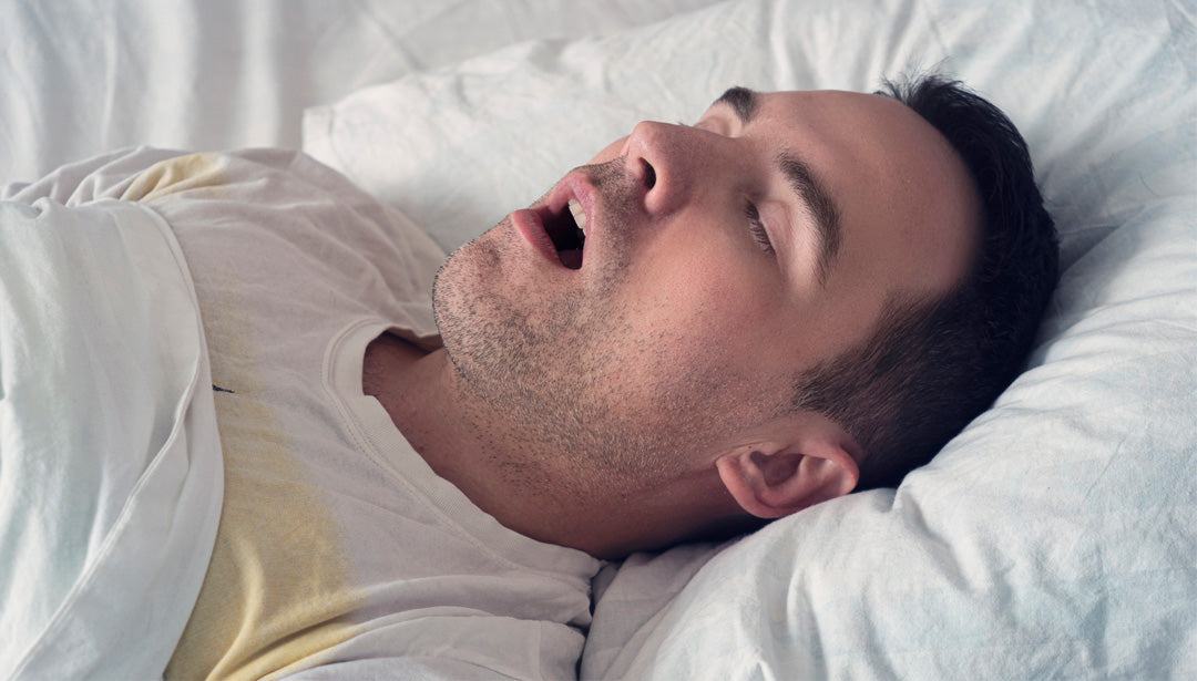 Ein dunkelhaariger Mann liegt schnarchend in einem Bett und schläft.