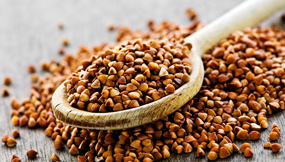 Samenkörner von Buchweizen liegen teils auf einem Tisch, teils auf einem Holzlöffel