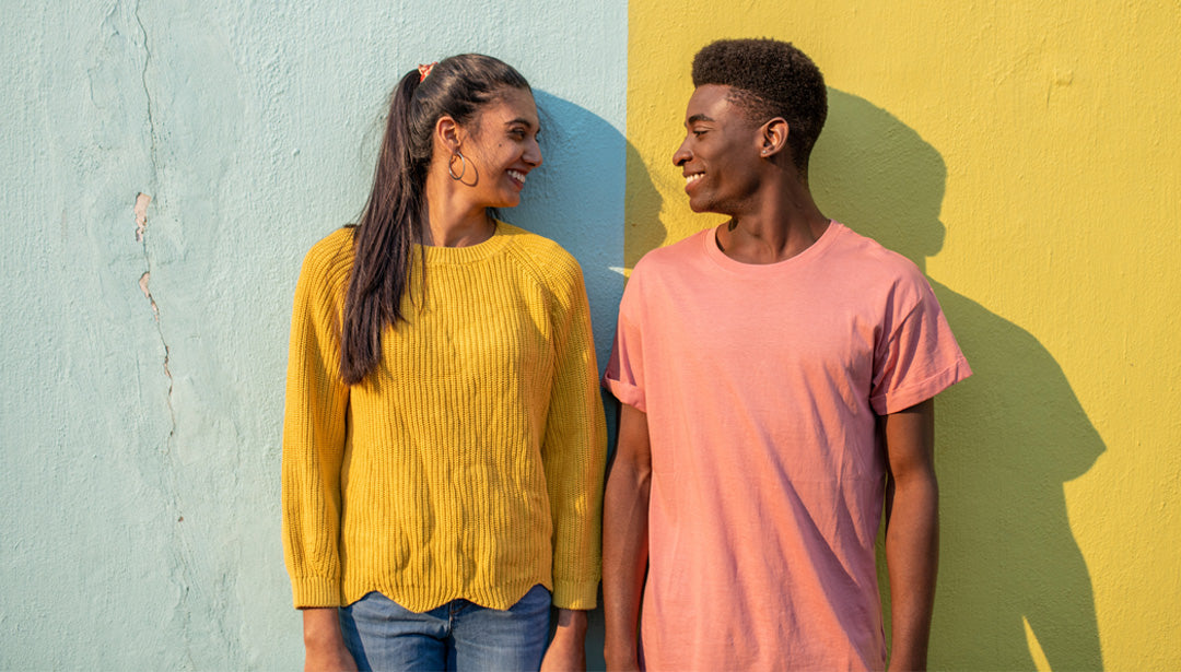 Eine junge Frau und ein junger Mann sthen vor einer Wand und schauen sich lächelnd an.