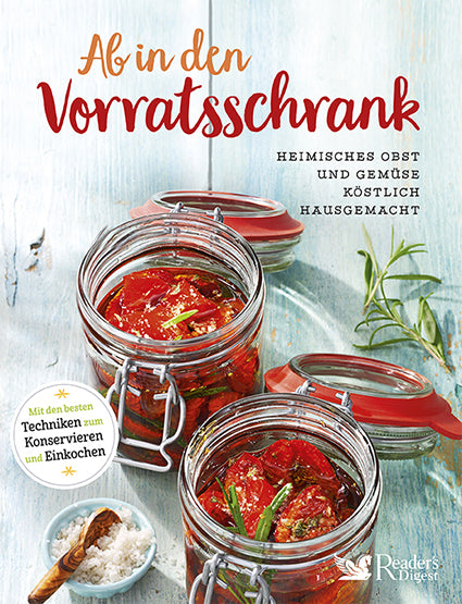 Two glass jars filled with vibrant, home-preserved sun-dried tomatoes and rosemary sit on a rustic table. A sprinkle of salt and the cookbook title "Ab in den Vorratsschrank" hint at delicious homemade recipes. 
